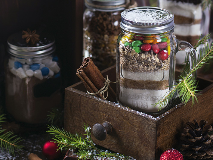 A jar of candy brownie mix in a wooden box with cinnamon sticks