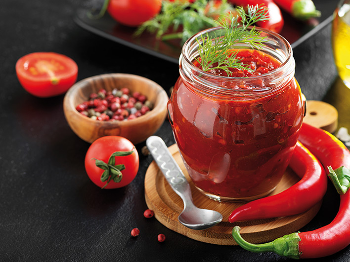 Chilli chutney in a glass jar with a spoon on a wooden board