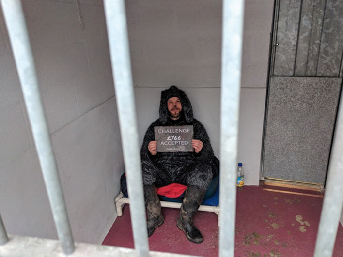 Man dressed as a dog sitting in a kennel for charity