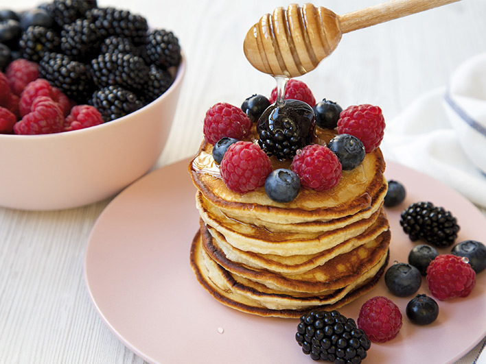 A pile of pancakes on a plate with friut and honey